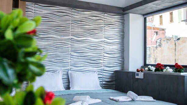 A modern hotel room with a bed, a window, and a decorative wall panel. - Kastren Rooms (Chania)