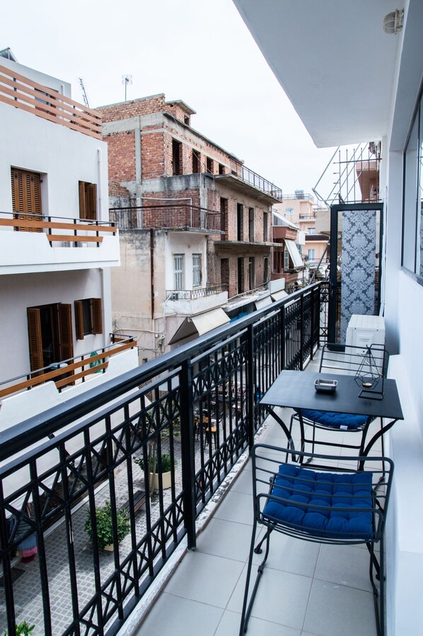 A balcony with a table and chairs, a view of neighboring buildings, and a railing.