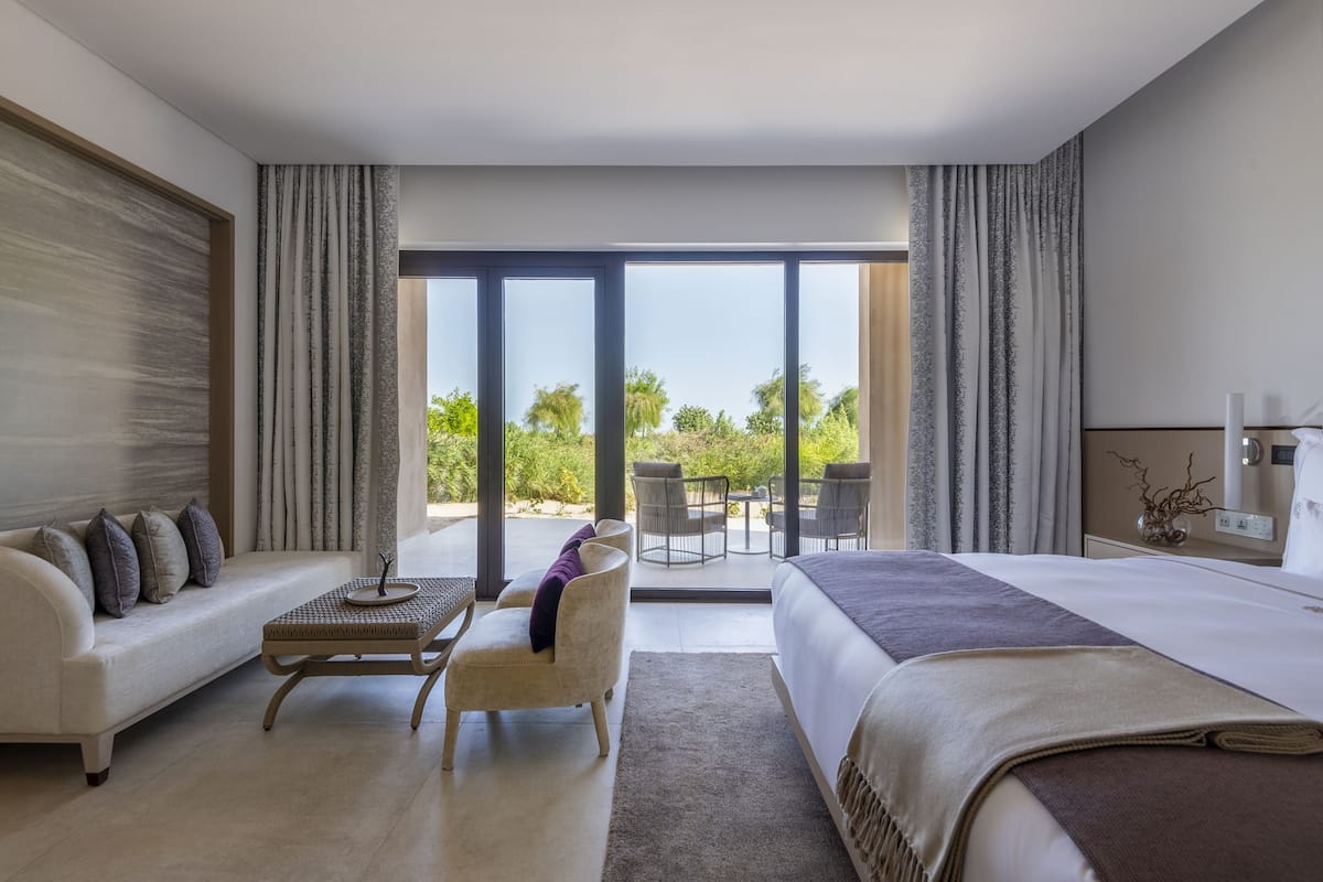 Une chambre d’hôtel moderne dotée d’un grand lit, d’un canapé, d’une petite table et d’un balcon avec une table et des chaises.