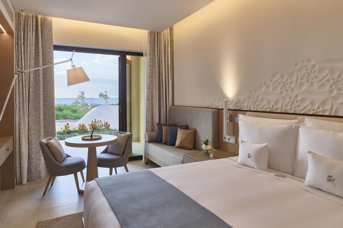 Een moderne hotelkamer met een groot bed, een slaapbank, een eettafel en uitzicht op zee.