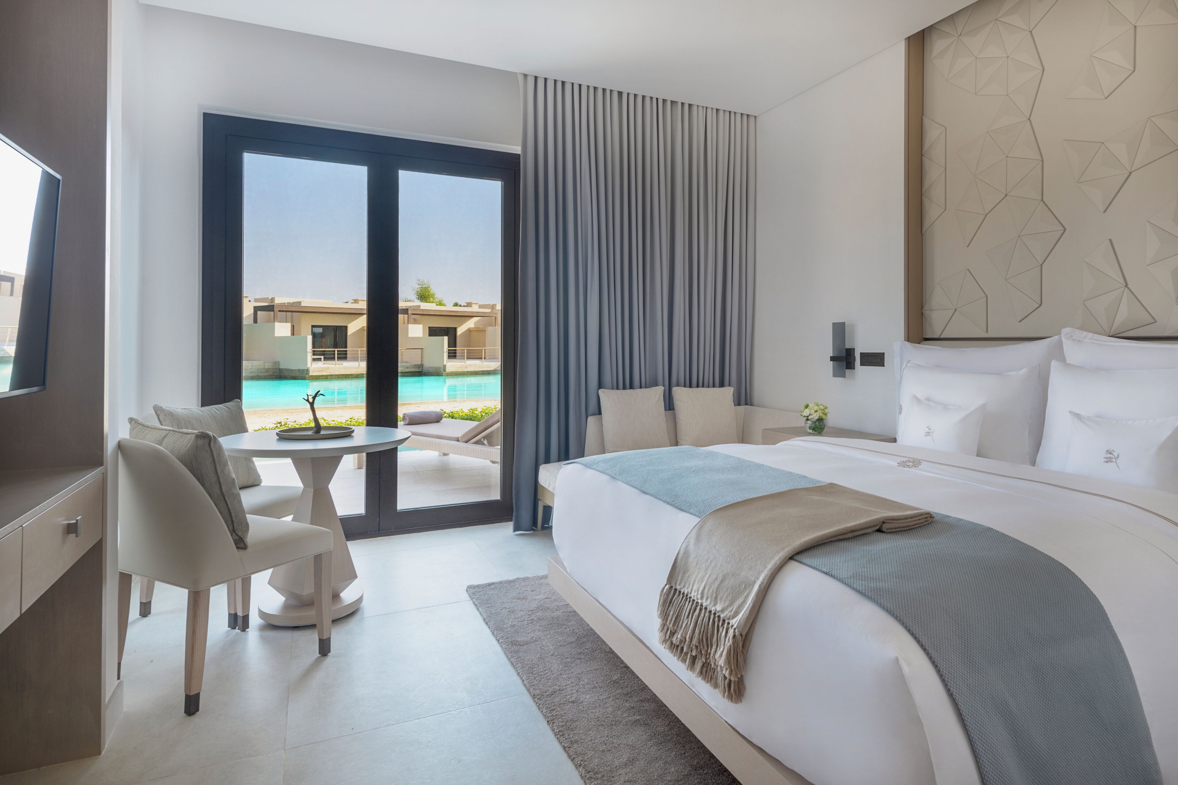 A modern hotel room with a large bed, a desk, and a view of a swimming pool.