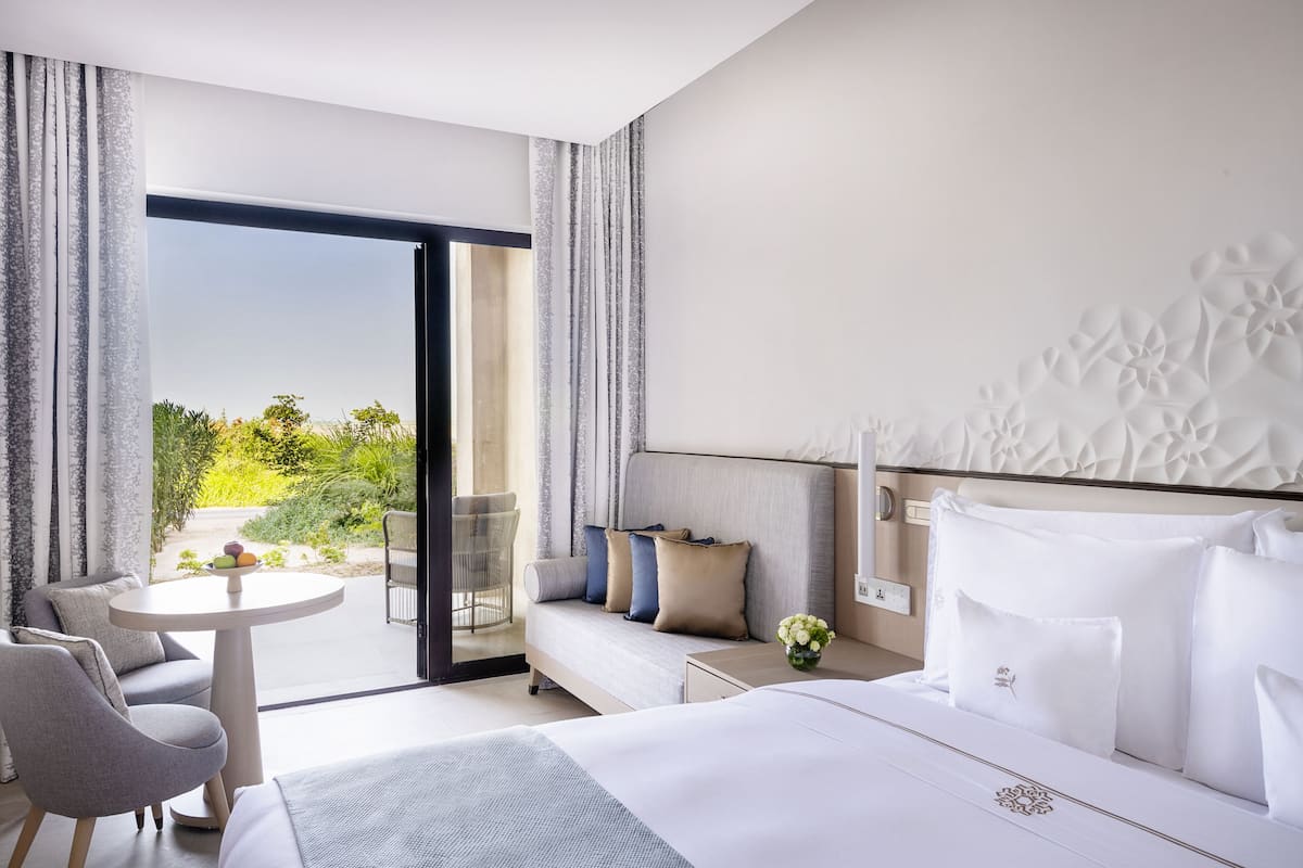 Une chambre d’hôtel moderne dotée d’un grand lit, d’un canapé, d’une petite table et d’un balcon offrant une vue sur la verdure.
