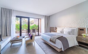 Een moderne hotelkamer met een groot bed, een zithoek met een tafel en stoelen, en uitzicht op het omliggende landschap via een schuifpui.