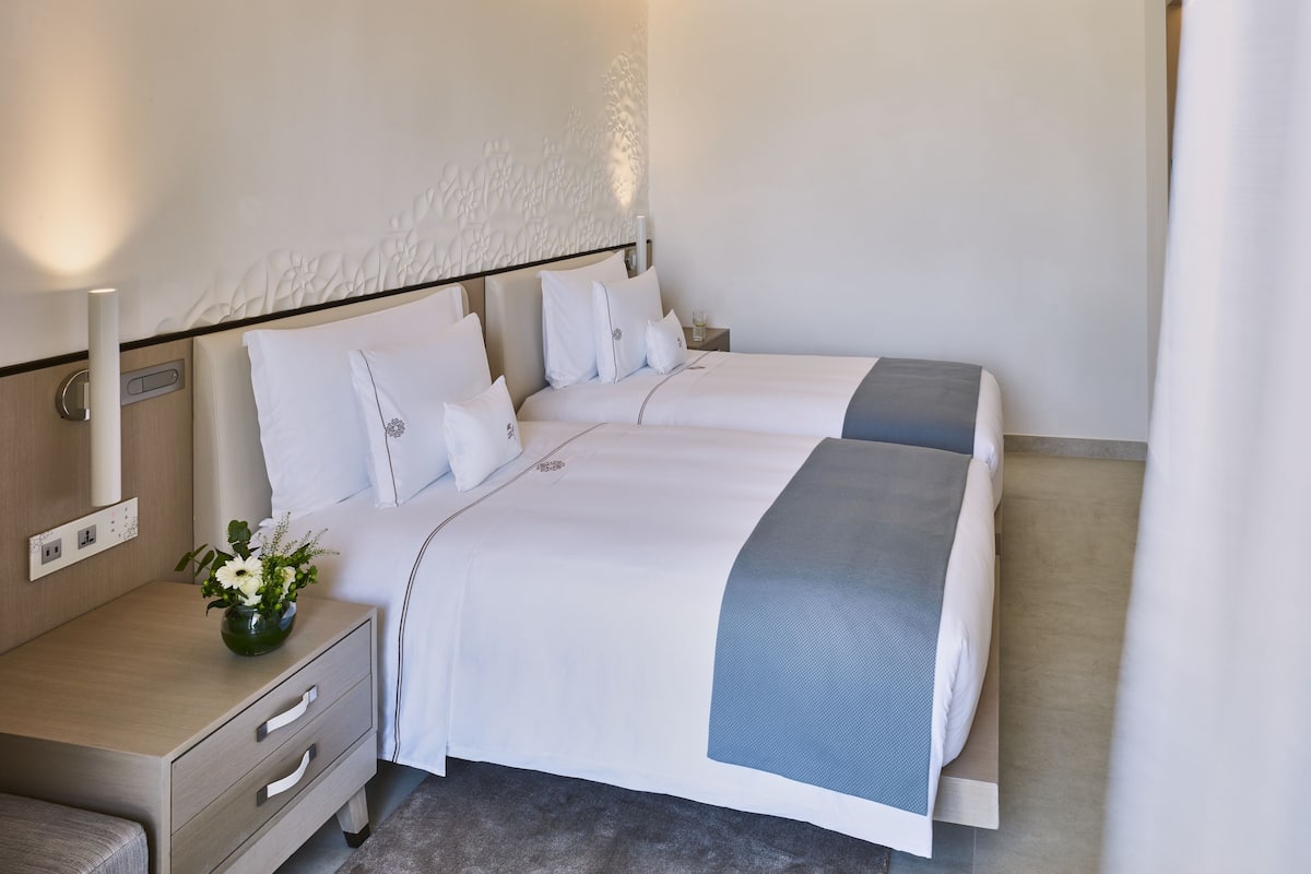 Une chambre d’hôtel avec un lit double, une table de chevet ornée d’un vase de fleurs et un luminaire fixé au mur.