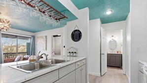 Una cocina moderna con armarios blancos, una isla grande con pileta y una estantería colgante para vinos.