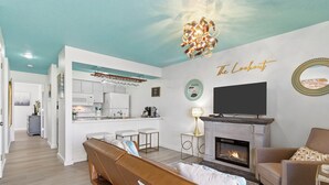 Una sala de estar moderna con chimenea, un sofá, un televisor y una cocina al fondo.