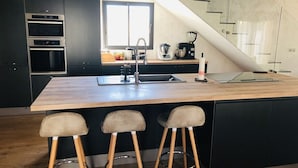 A modern kitchen with a large island, bar stools, and a staircase leading to an upper level. - Villa design swimming pool Avignon festival (Avignon)
