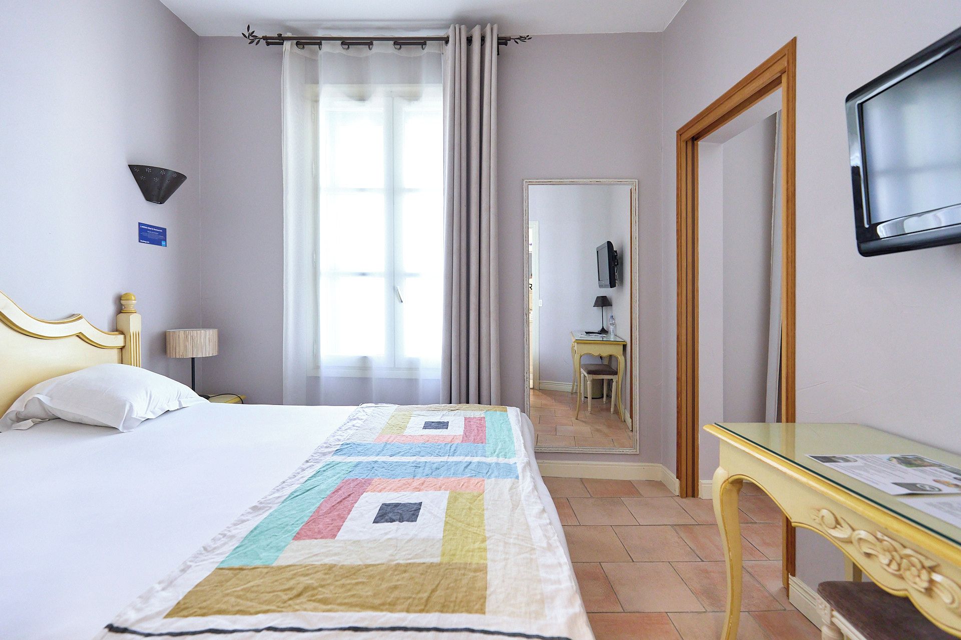 A hotel room with a bed, a desk, a chair, a television, and a mirror.