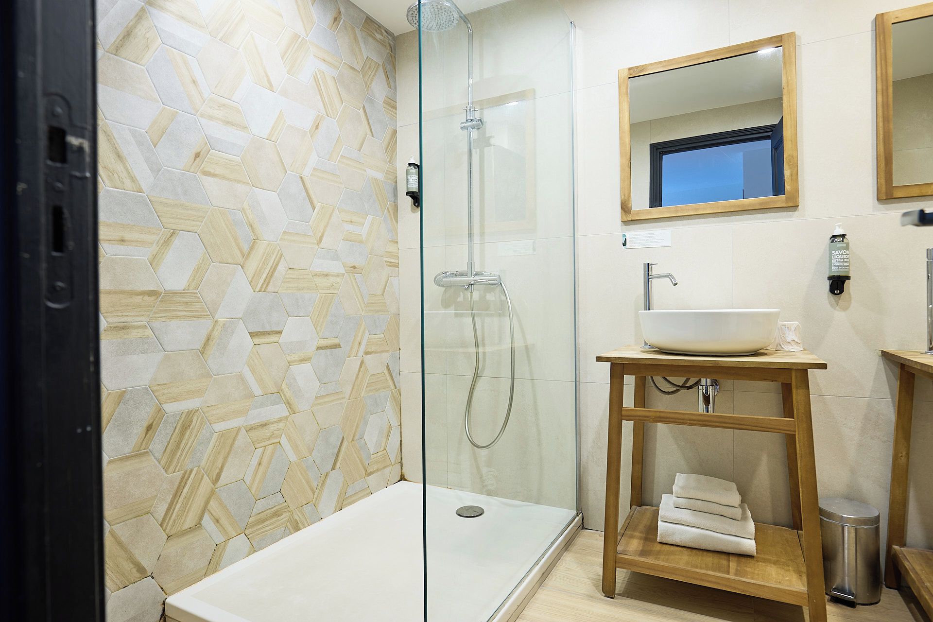 A modern bathroom with a glass shower enclosure, a white sink, and a wooden vanity.