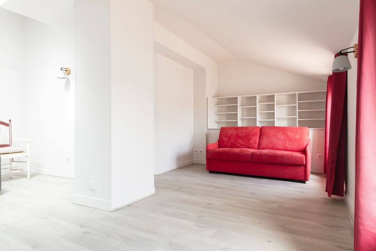 Una sala moderna con un sofá rojo, estantería blanca y una mesa de comedor blanca.