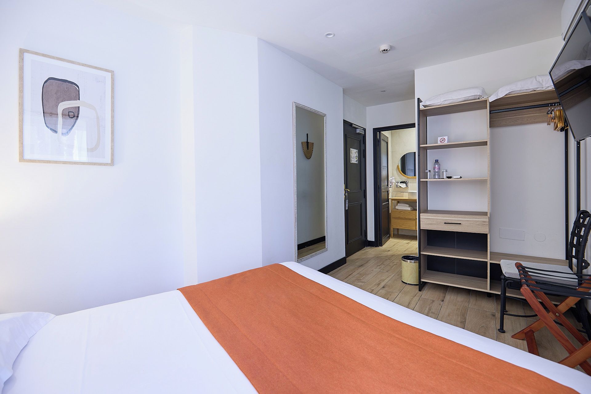 A hotel room with a bed, a wardrobe, a mirror, and a framed picture on the wall.