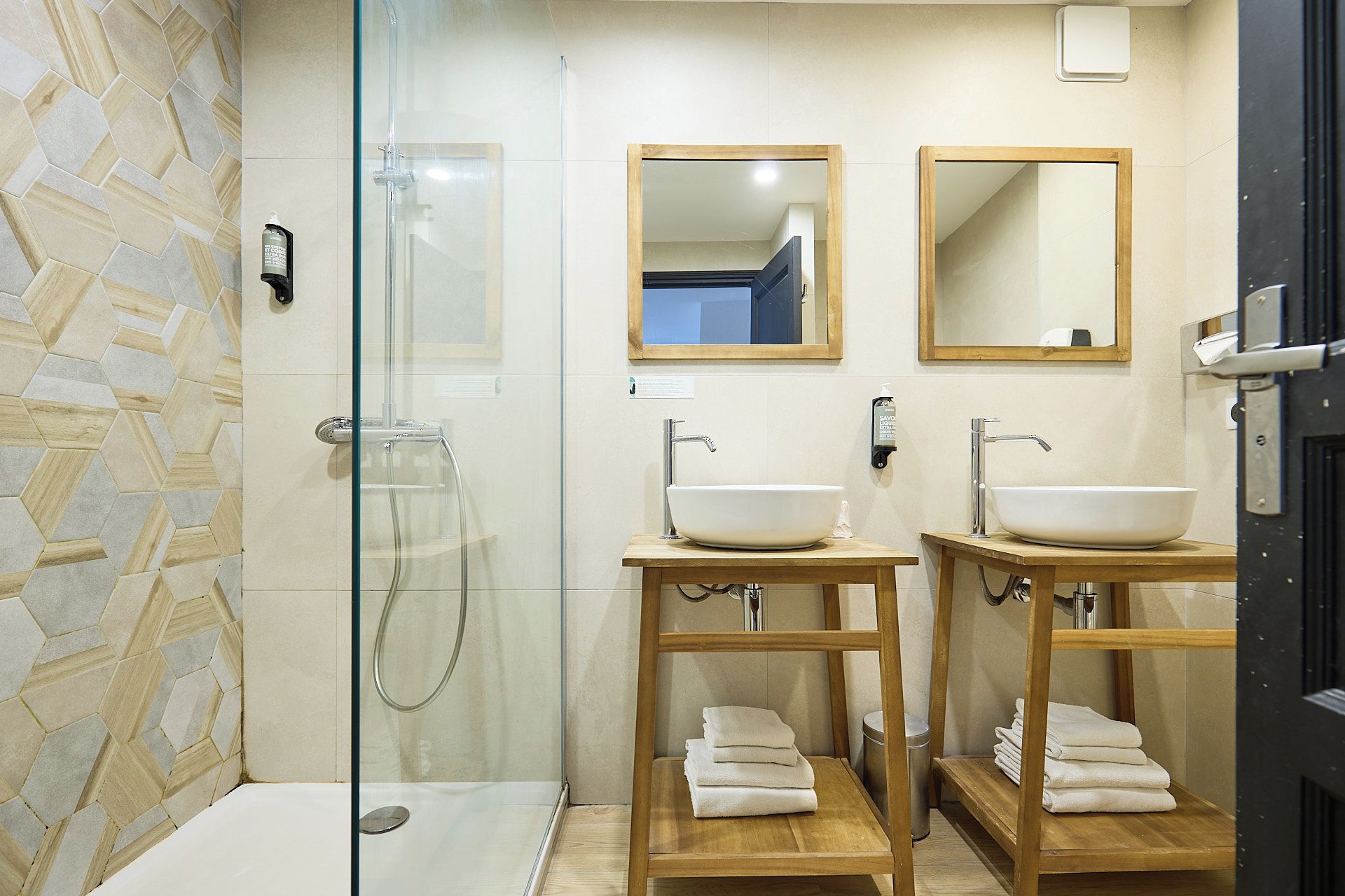 A bathroom with a glass-enclosed shower, two sinks with wooden pedestals, and a mirror above each sink.
