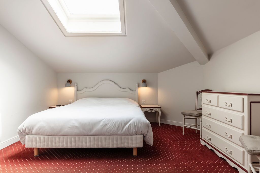 Een slaapkamer met een bed, een dressoir, twee nachtkastjes en een dakraam.