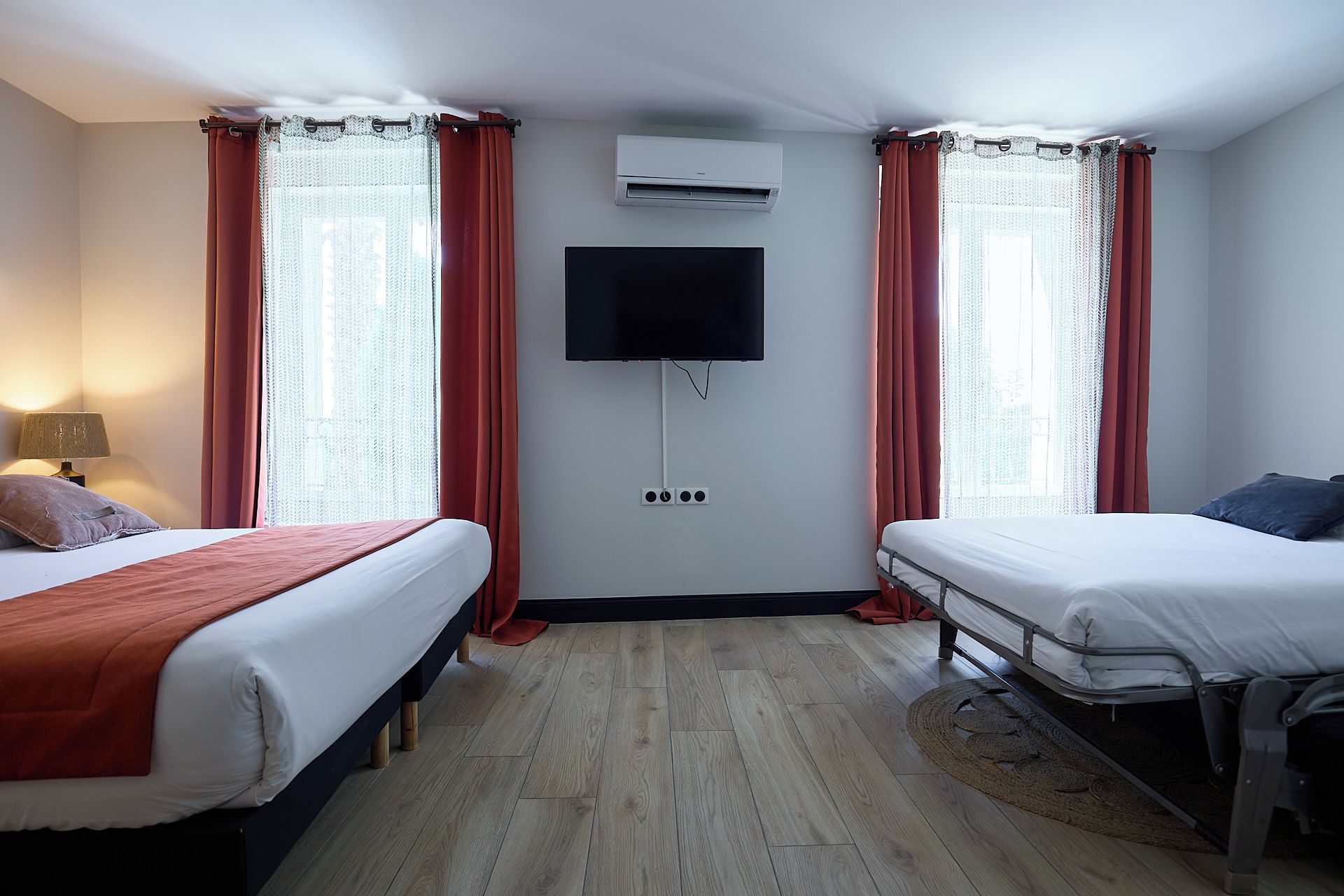 A hotel room with two beds, a flat-screen TV mounted on the wall, and an air conditioning unit.