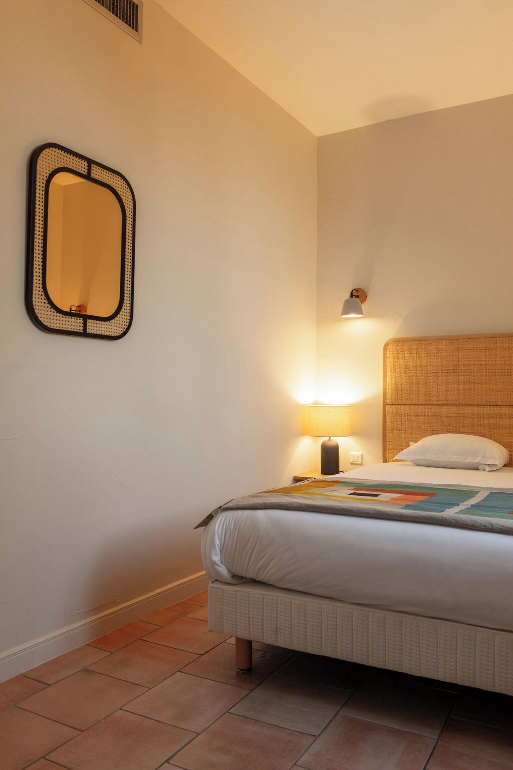 Une chambre d’hôtel avec un lit, un miroir fixé au mur, une lampe de chevet et une tête de lit.