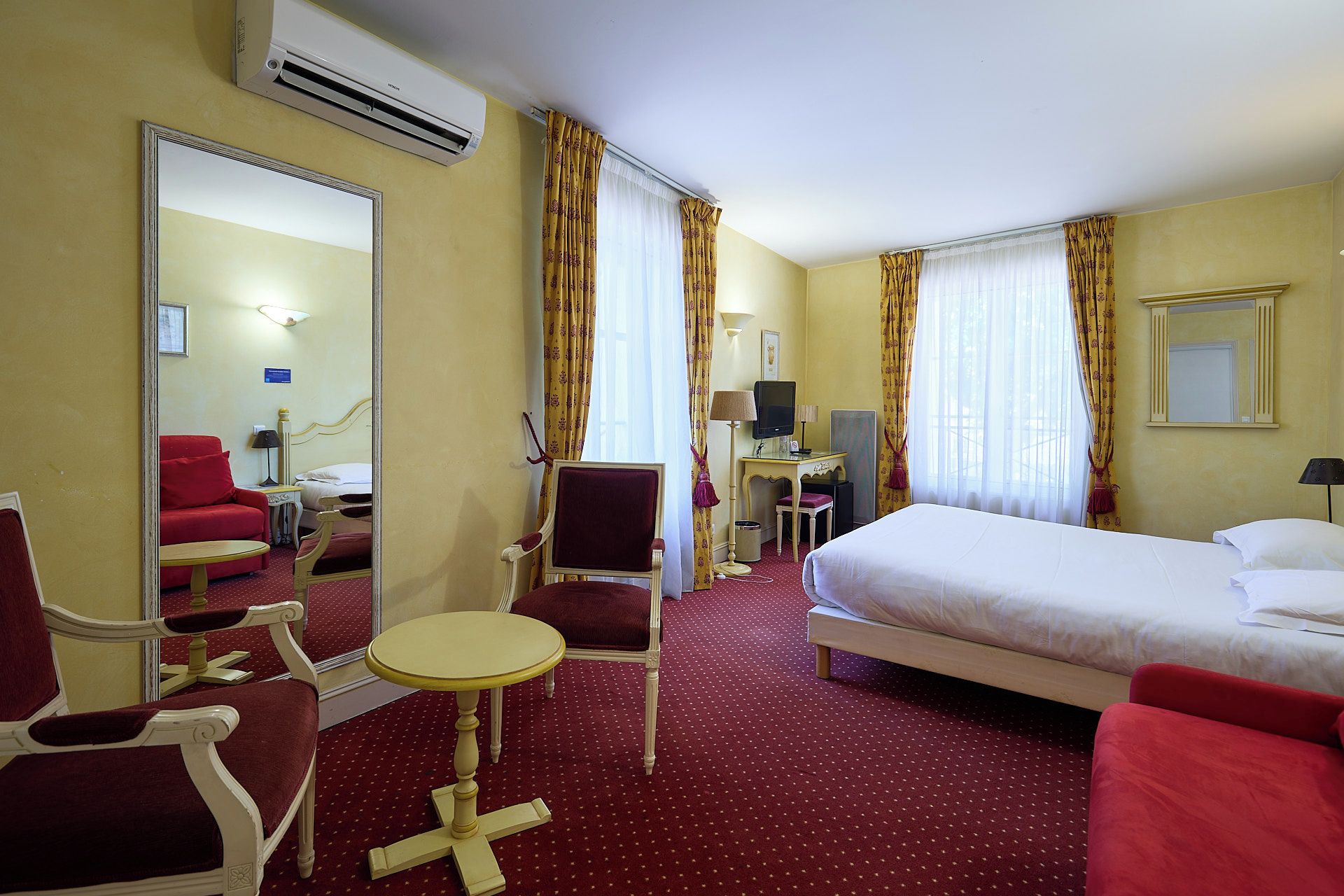 A hotel room with a bed, a desk with a computer, a chair, a small table, and a mirror.