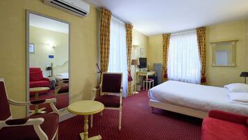A hotel room with a bed, a desk with a computer, a chair, a small table, and a mirror.