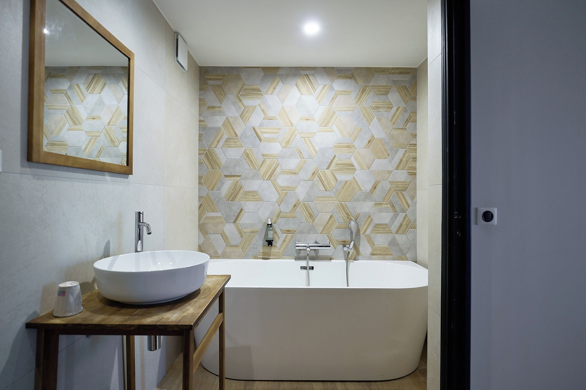 A modern bathroom with a freestanding bathtub, a round sink on a wooden table, and a geometric patterned wall.