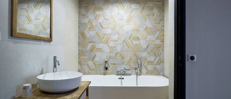 A modern bathroom with a freestanding bathtub, a round sink on a wooden table, and a geometric patterned wall.