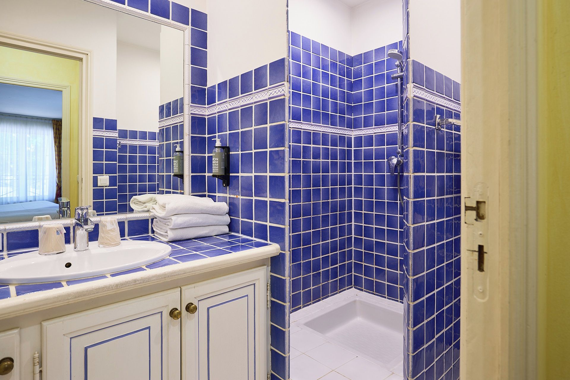 A bathroom with a sink, mirror, and blue-tiled shower enclosure.