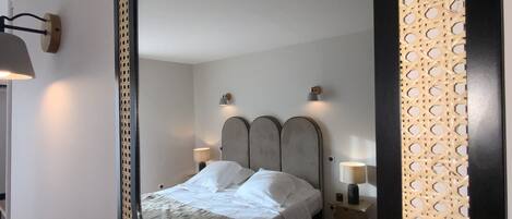 A bedroom with a bed, two bedside lamps, a wall-mounted mirror, and a decorative wall panel.