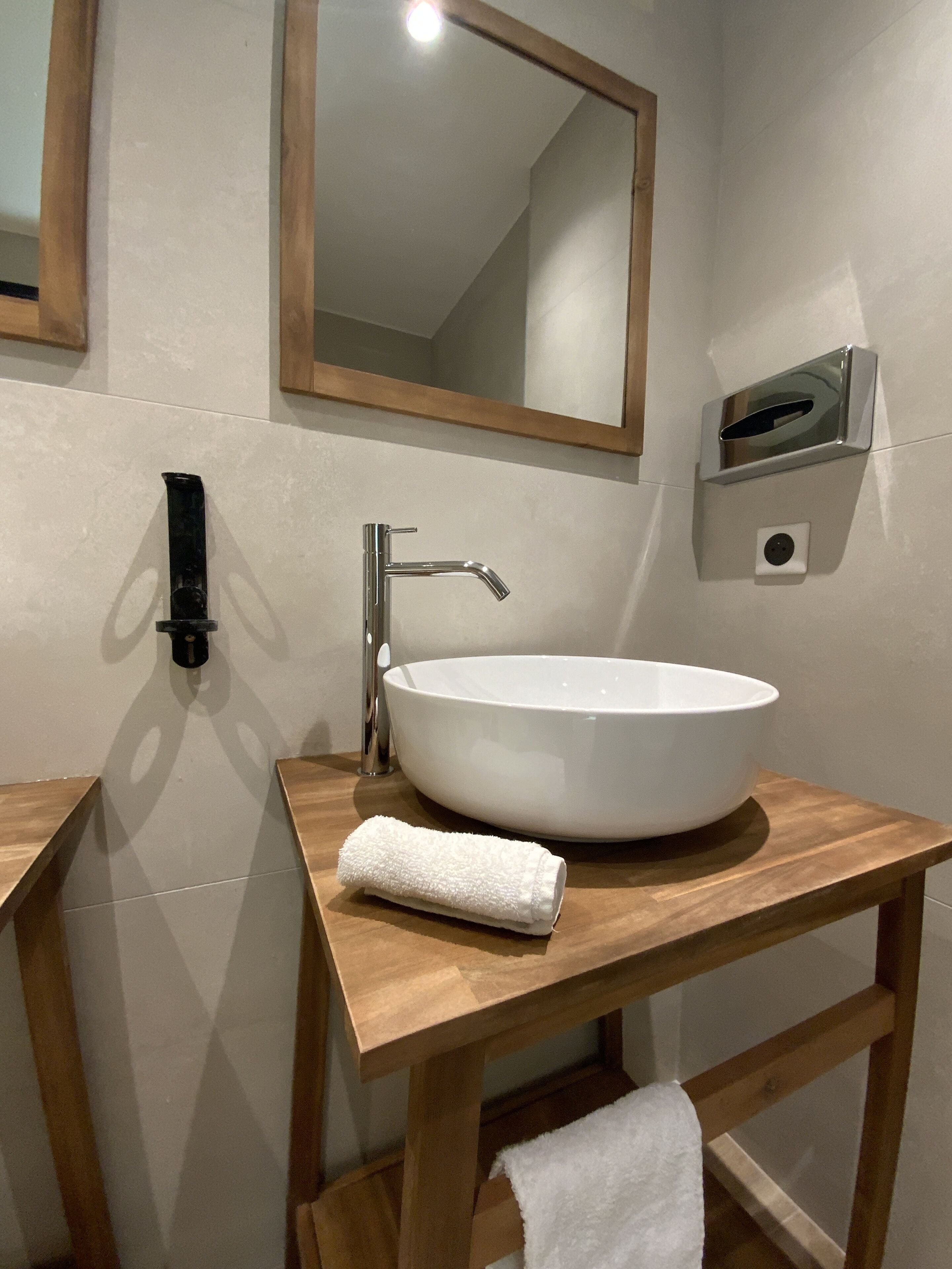 Un baño con un lavabo blanco, un mueble de tocador de madera, un espejo y un dispensador de toallas.
