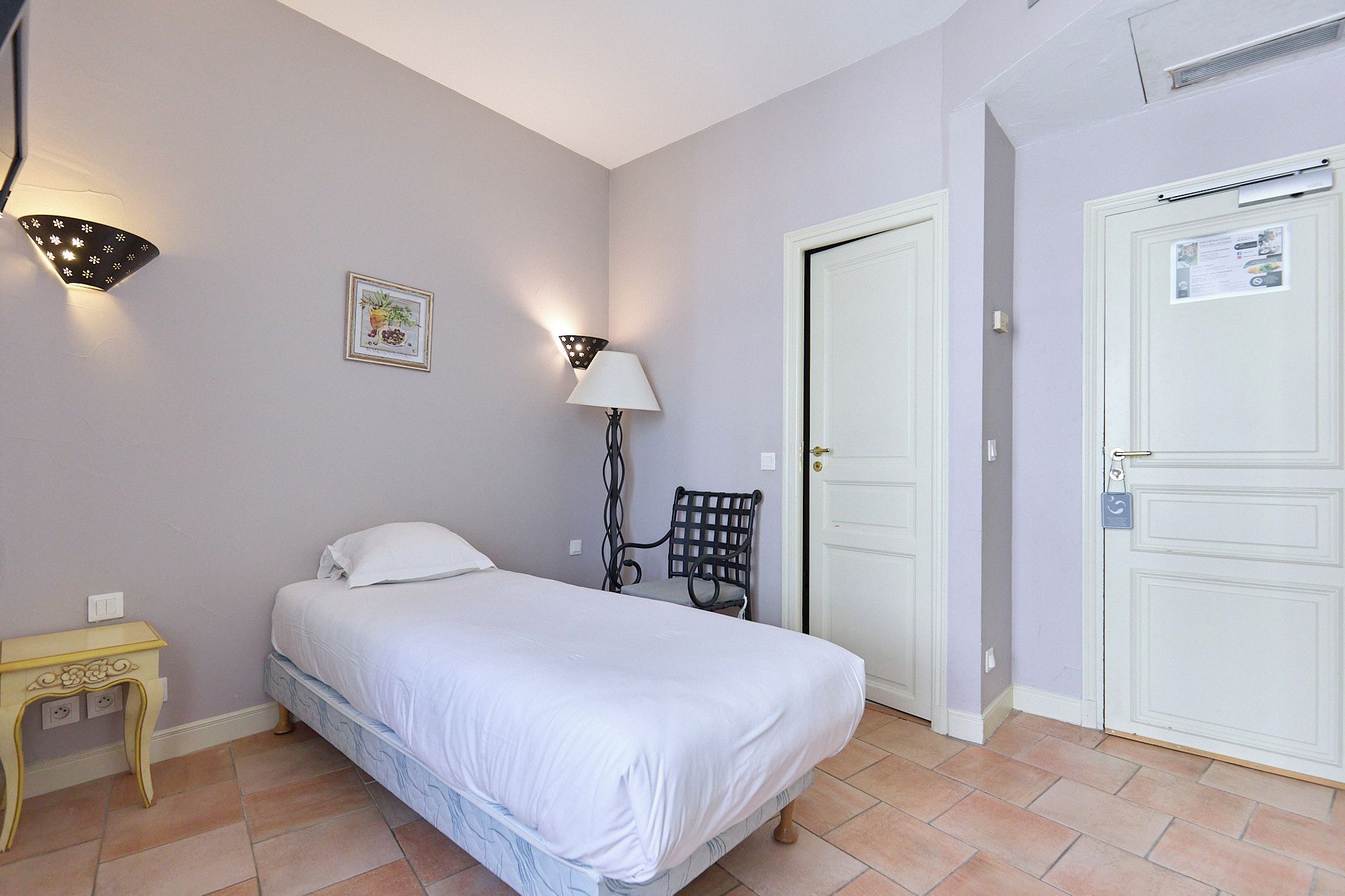 Un dormitorio con cama, lámpara de noche, silla y dos puertas.