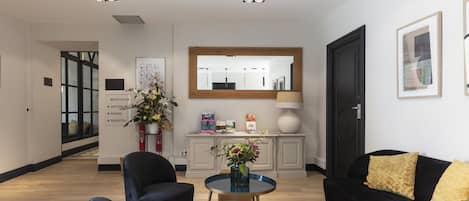 A modern hotel lobby with a reception desk, a black sofa, and a round table with a vase of flowers.