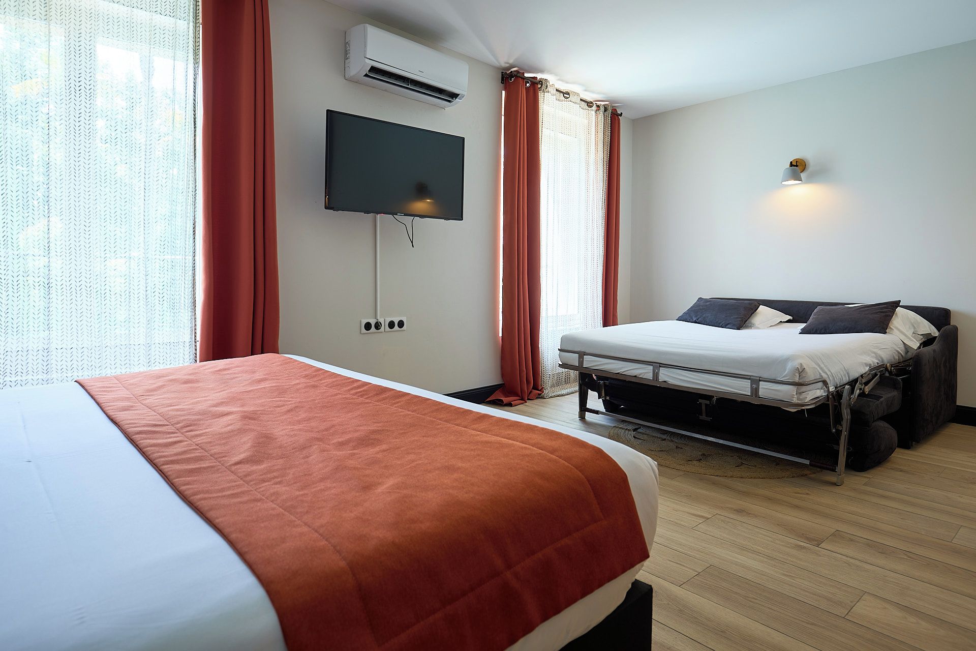 A hotel room with a bed, a TV mounted on the wall, and a bedside table.