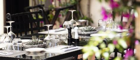 Un espace de restauration en plein air avec des tables pour deux personnes, entouré de chaises en osier noir.