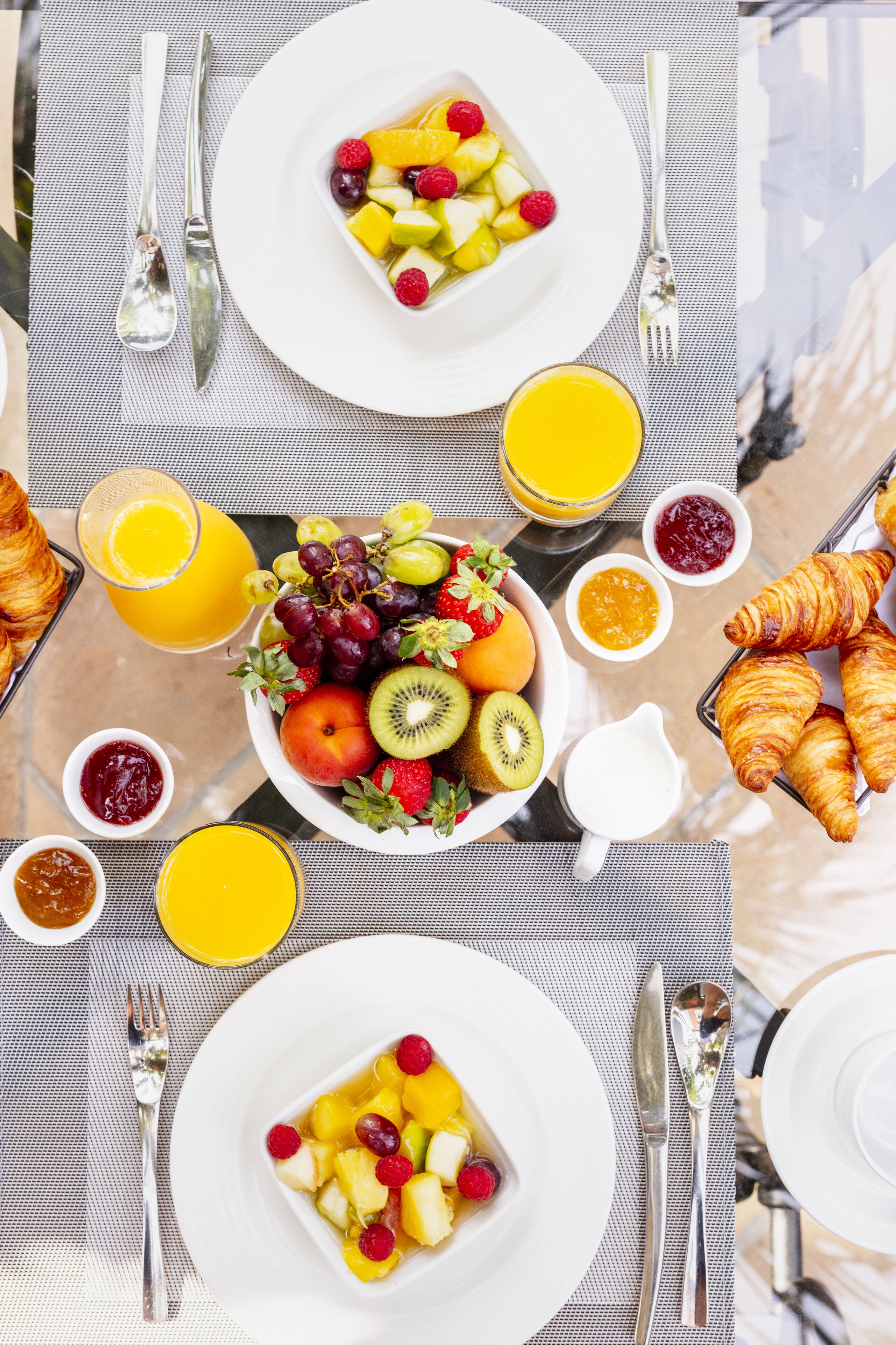 A breakfast setting with plates of fruit, croissants, and juice.