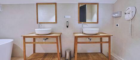 A bathroom with two wooden vanity tables, each with a white sink and a mirror above. There is a hairdryer on the wall to the right.