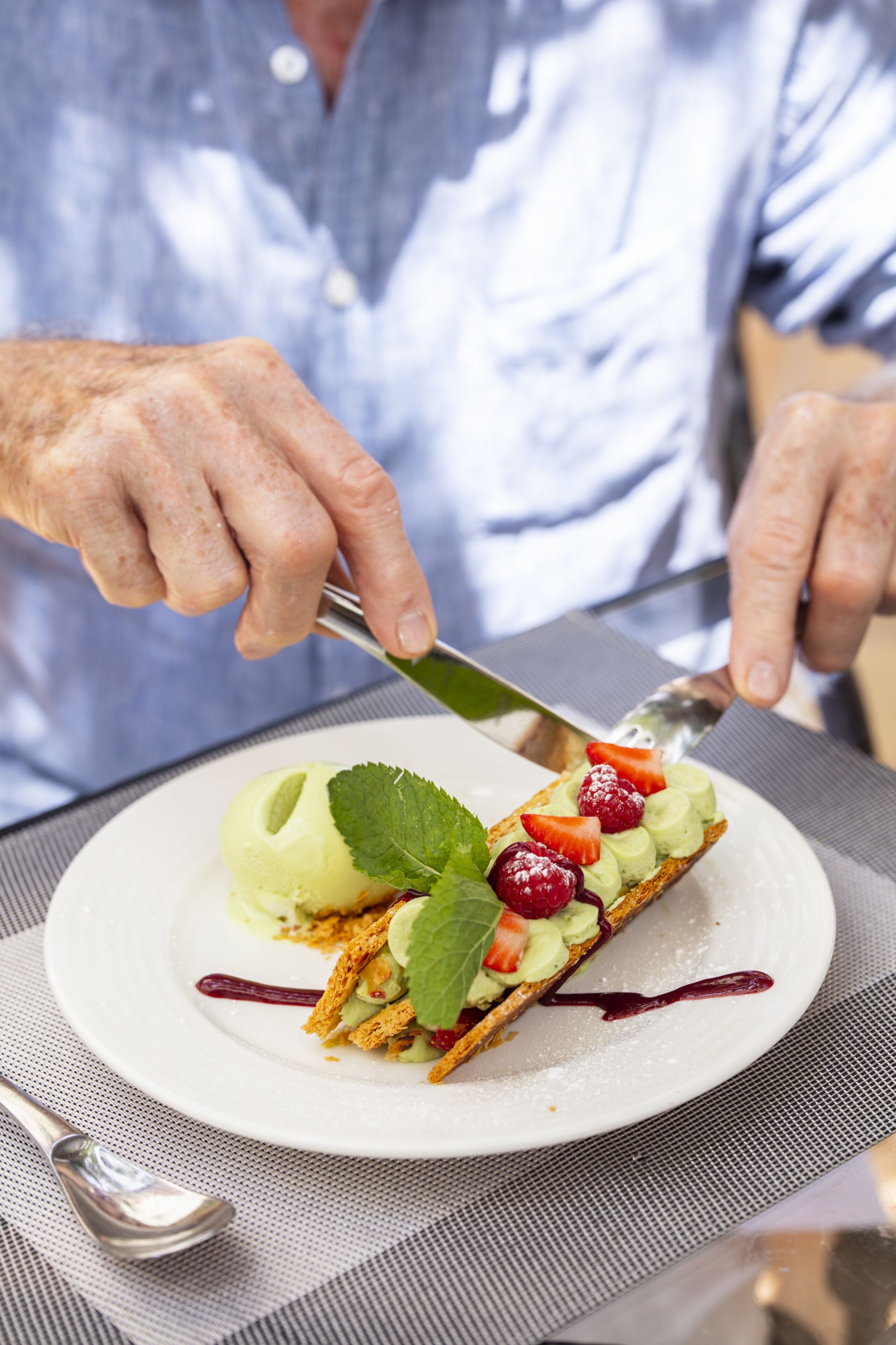Una persona cortando un postre con un cuchillo sobre un plato blanco.
