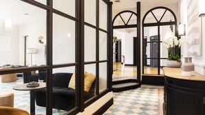 A modern hotel lobby with a checkered floor, a black sofa with a yellow pillow, and a large window with black framing. - Hôtel l'Arena (Fréjus)