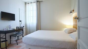 A hotel room with a bed, a desk with a chair, a television, and a wall-mounted lamp.
