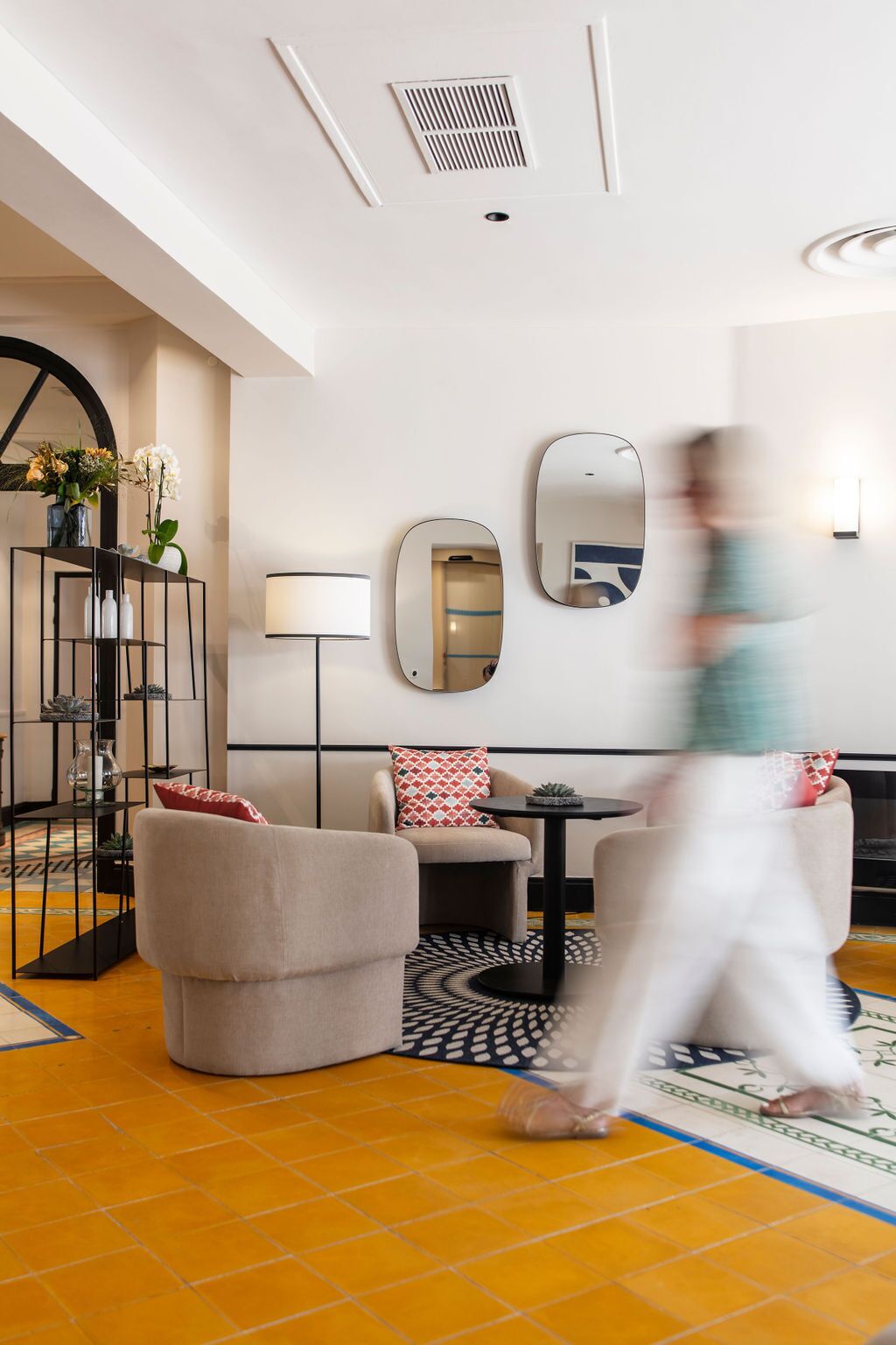 Un moderno vestíbulo de hotel con una zona de estar, una lámpara de pie y un espejo decorativo.