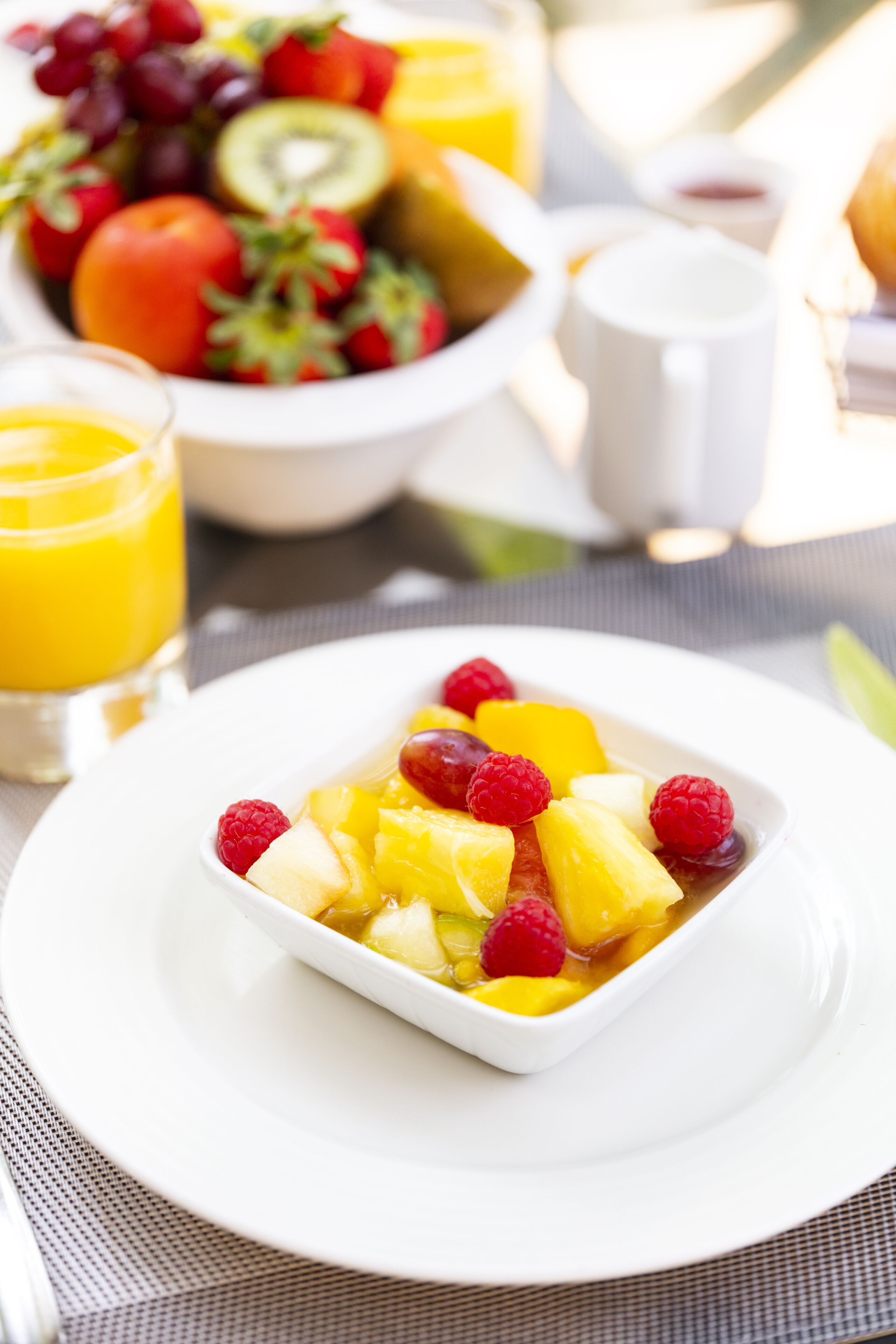 Un desayuno con una ensalada de frutas, un vaso de zumo de naranja y tostadas.