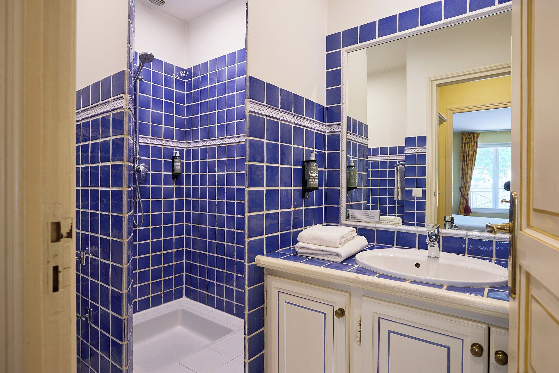 A bathroom with blue-tiled walls, a white bathtub, a sink, and a mirror.