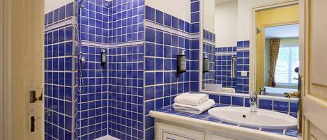 A bathroom with blue-tiled walls, a white bathtub, a sink, and a mirror.
