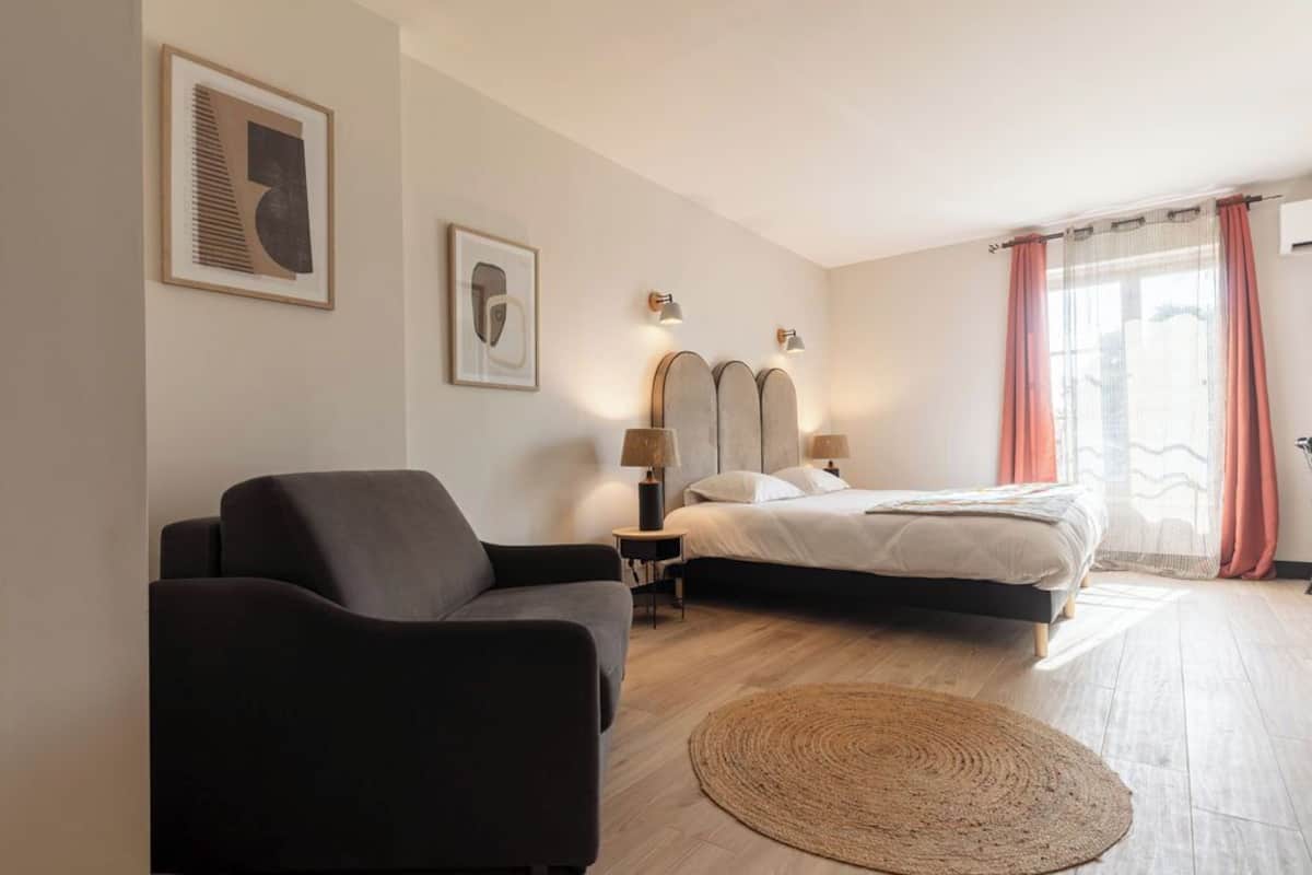 Un dormitorio con una cama, un sofá, dos lámparas de pared y una alfombra tejida.