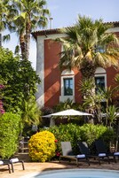 Zona junto a la piscina con sillones de descanso, una palmera y un edificio de fachada roja.