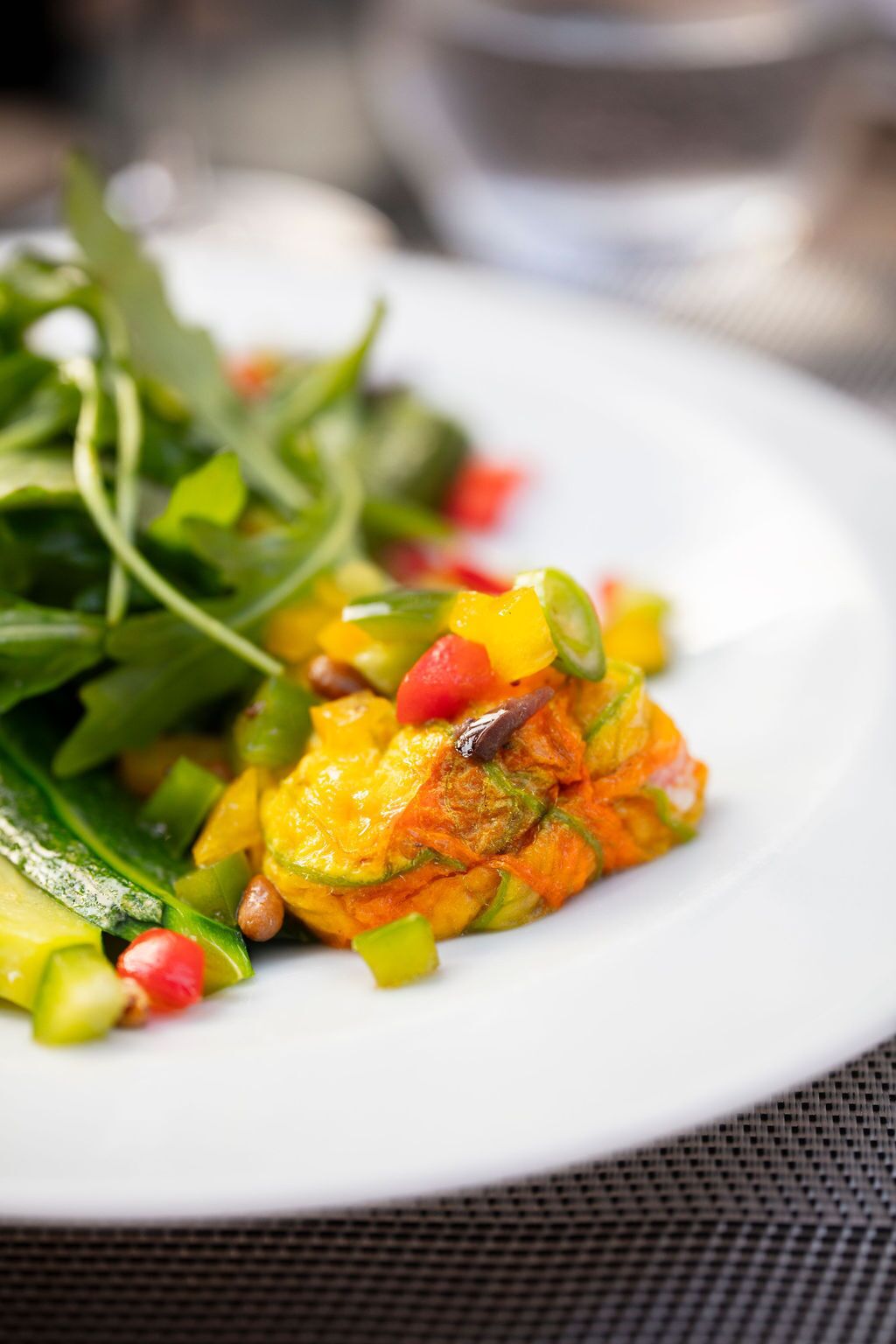 A plate with a colorful vegetable dish, possibly containing zucchini, bell peppers, and pomegranate seeds, served on a white plate.