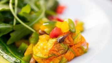A plate with a colorful vegetable dish, possibly containing zucchini, bell peppers, and pomegranate seeds, served on a white plate.