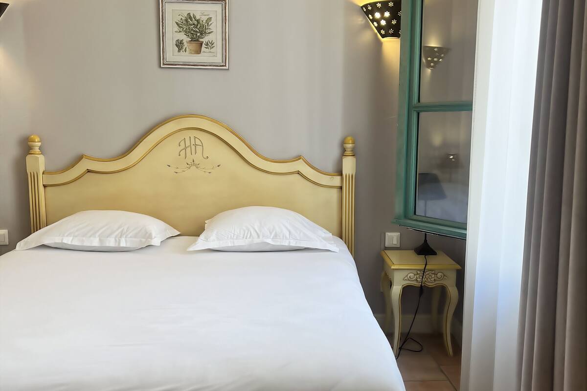Una cama con cabecera dorada, ropa de cama blanca y una mesita de noche pequeña con una lámpara.