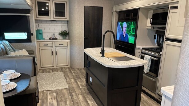 A compact kitchen with a built-in island, white cabinets, a black countertop, and a television. - "Gone Coastal" Luxury Glamper by the Beach (Carrabelle)