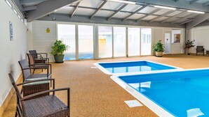An indoor swimming pool with a tiled floor, large windows, and wicker chairs. - Serendipity Lodge (Torpoint)