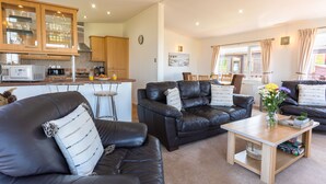A modern living room with leather sofas, a coffee table, and a kitchen area with wooden cabinets and a microwave. - Serendipity Lodge (Torpoint)