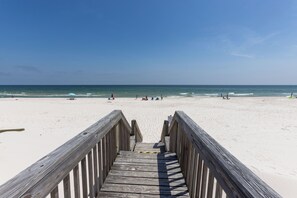 A wooden boardwalk leading to a sandy beach with clear skies.
