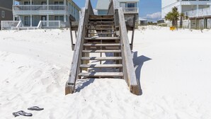 Un escalier en bois mène à une propriété située en bord de mer, dotée de plusieurs balcons et d’un toit bleu.
