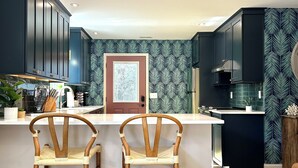 Una cocina moderna con armarios oscuros, una isla central, dos sillas de madera y un papel tapiz estampado.